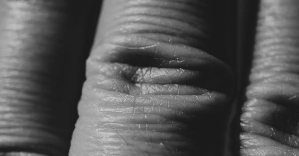 Prise de vue macro détaillée mettant en valeur la texture et le motif intriqués de la peau humaine ridée en noir et blanc.