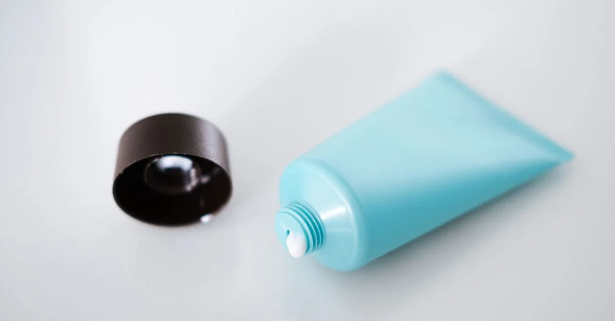Tube cosmétique bleu ouvert avec couvercle noir sur une surface claire, style minimaliste.