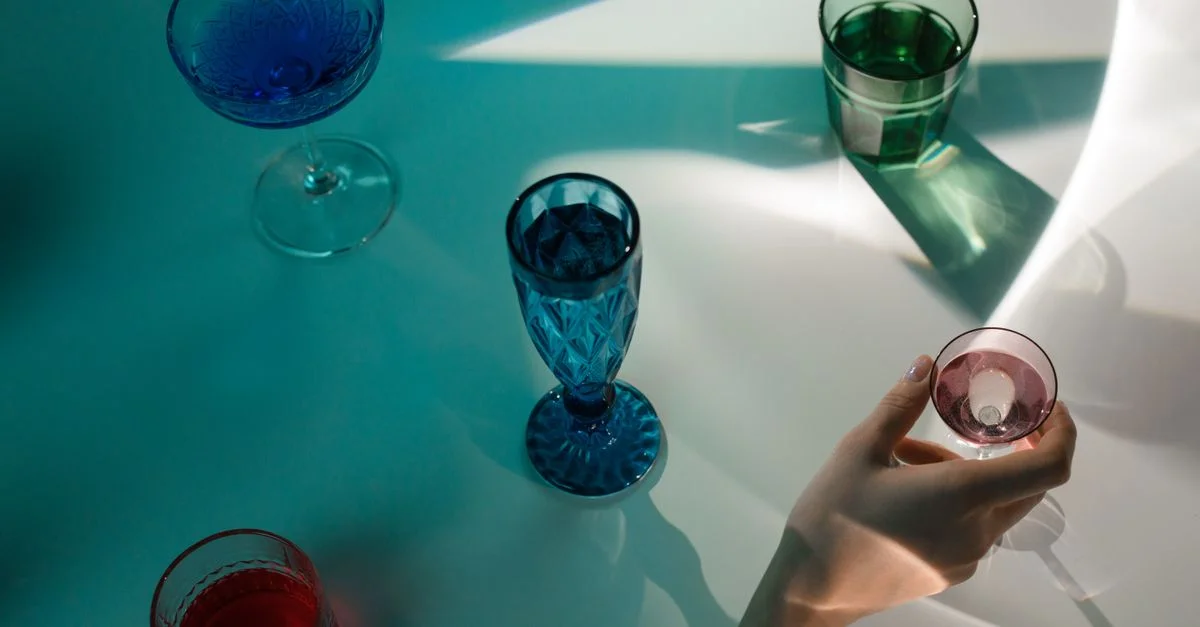 Arrangement élégant de verres colorés projetant des ombres sur une surface réfléchissante.