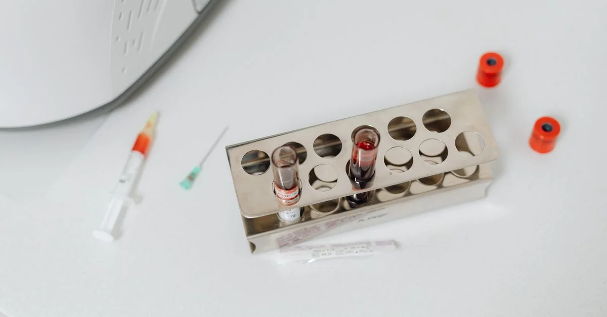 Prise de vue en plongée d'éprouvettes de laboratoire et d'une seringue sur une surface blanche, parfait pour des thèmes scientifiques et médicaux.