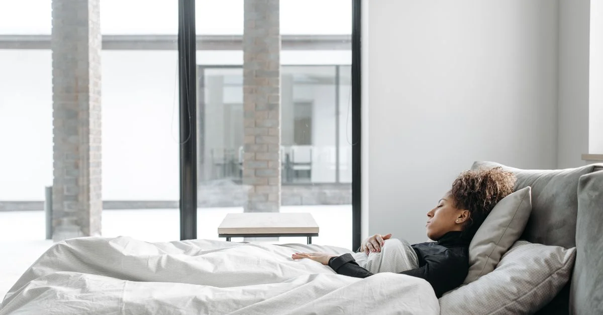 Une femme se repose confortablement dans un lit dans une pièce lumineuse et minimaliste.