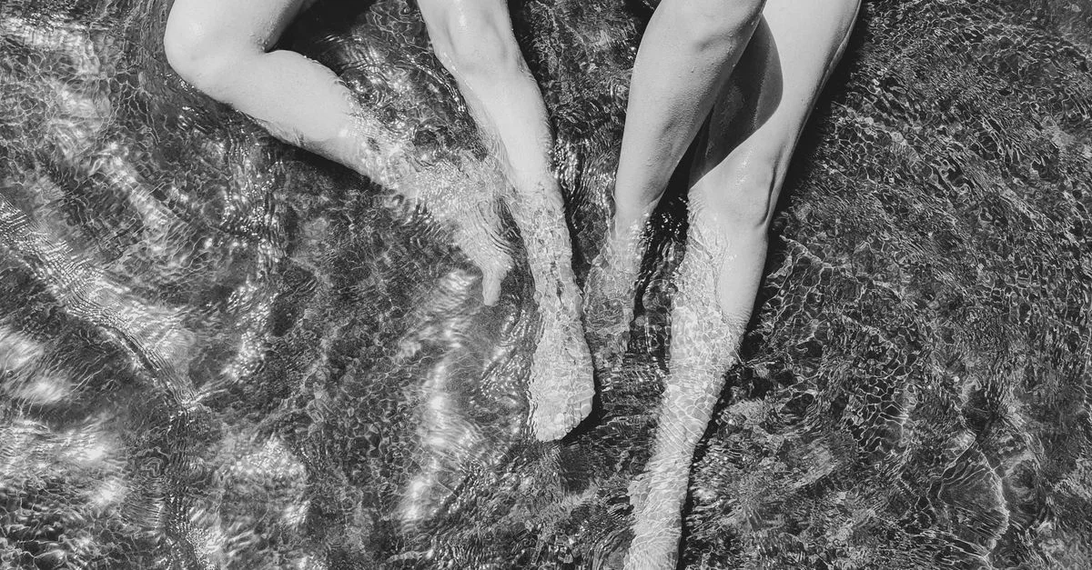 Jambes de deux femmes se relaxant dans l'eau dans un style artistique noir et blanc.