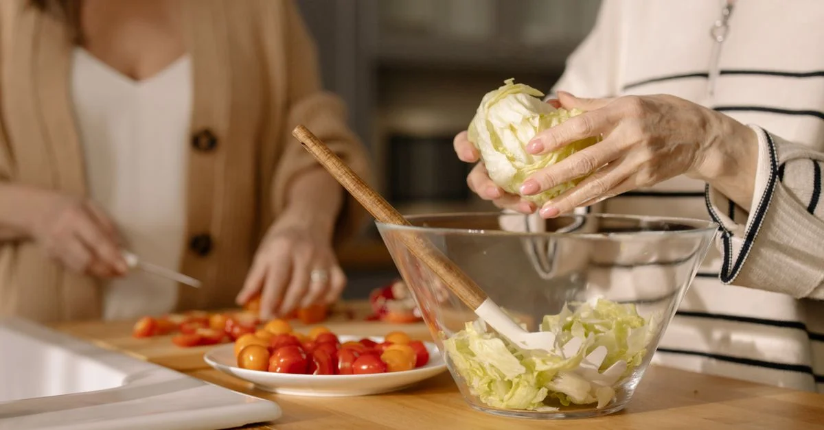 Deux femmes coupent des légumes frais pour une salade dans une cuisine moderne.