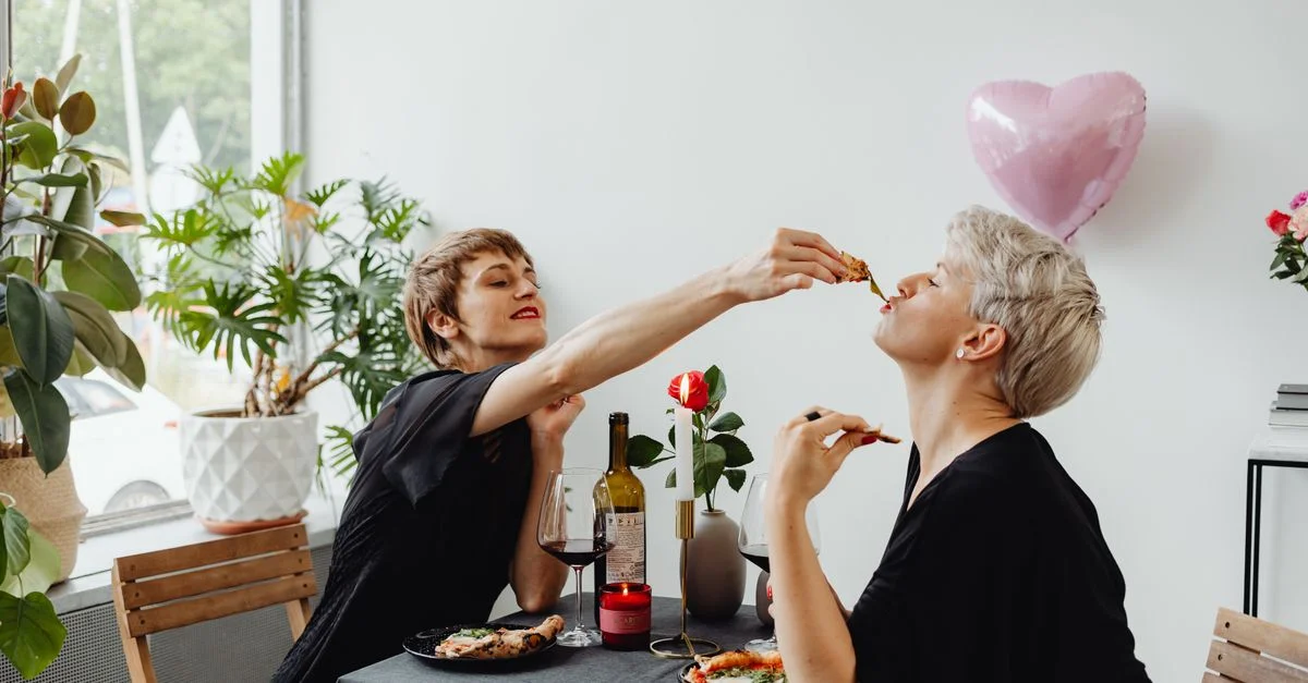 Un couple de femmes amoureuses profitant d'un repas romantique à l'intérieur avec du vin et un ballon en forme de cœur.
