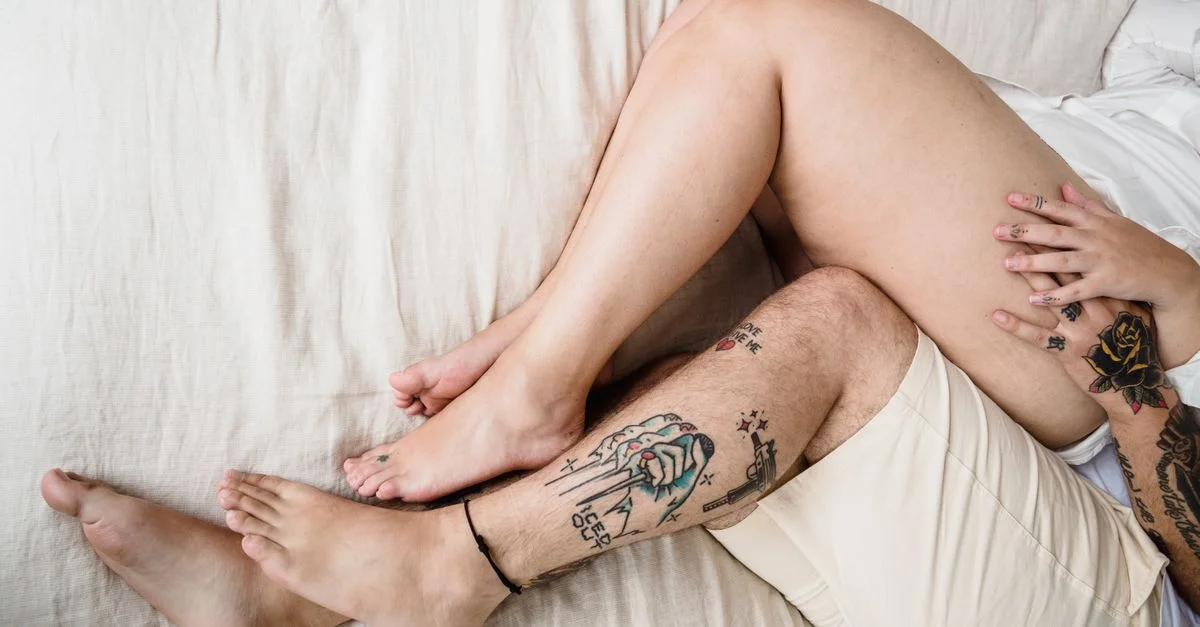 Gros plan des jambes tatouées d'un couple s'entrelacent sur le lit à la lumière du jour.