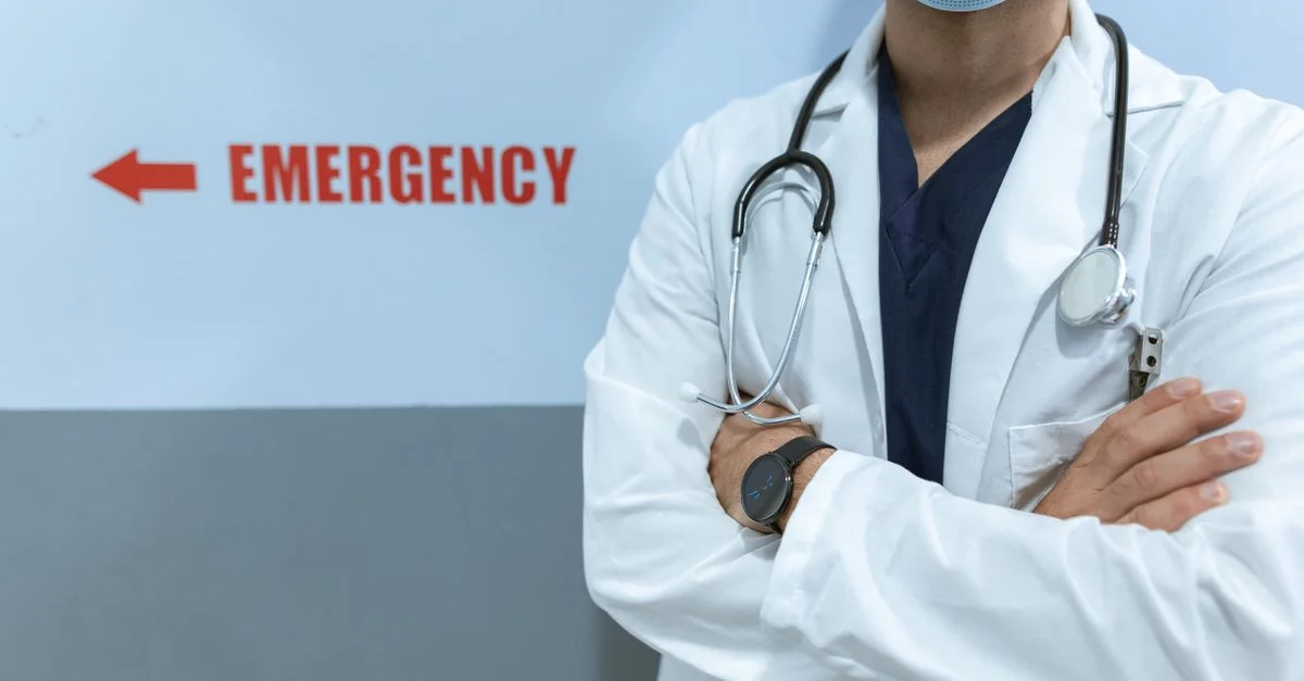 Travailleur de la santé dans une salle d'urgence avec un stéthoscope et un masque facial, posture les bras croisés.