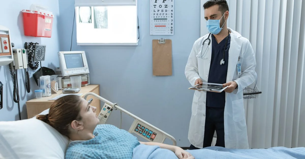 Médecin portant un masque facial consultant un patient dans une chambre d'hôpital, mettant en avant la sécurité en santé.