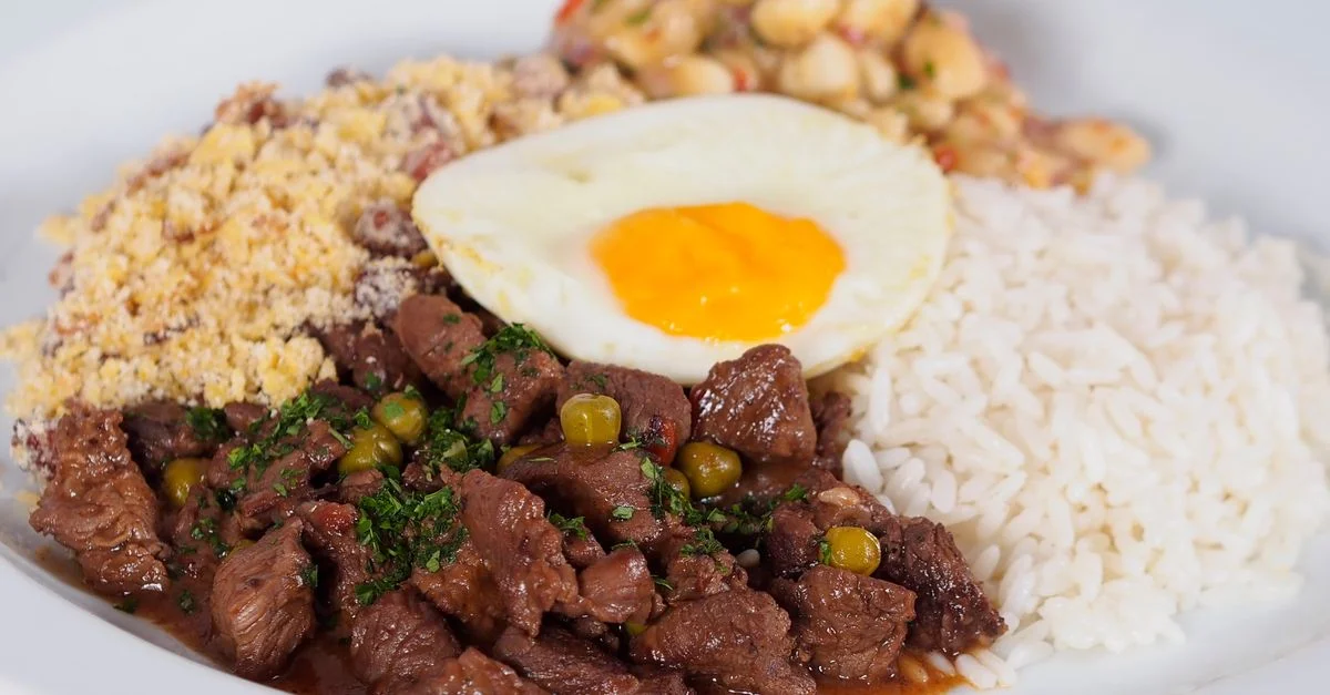 Une assiette de feijoada brésilienne avec du riz, des haricots, de la farofa et un œuf au plat.