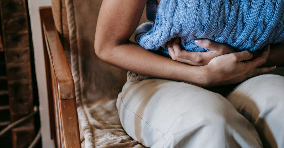 Une femme assise dans une pièce, tenant un coussin contre son ventre, indiquant un inconfort ou une douleur.