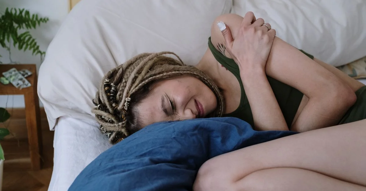 Une femme aux dreadlocks allongée sur le lit tenant son ventre de douleur, probablement à cause de crampes.
