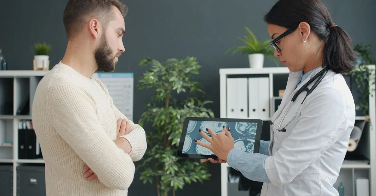 Dans une clinique moderne, un médecin montre une IRM à un patient inquiet à l'aide d'une tablette.