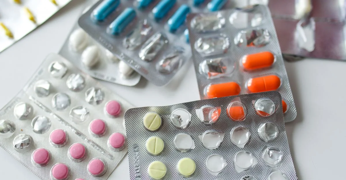 Assortiment de plaquettes de médicaments colorées et de capsules sur une surface blanche.