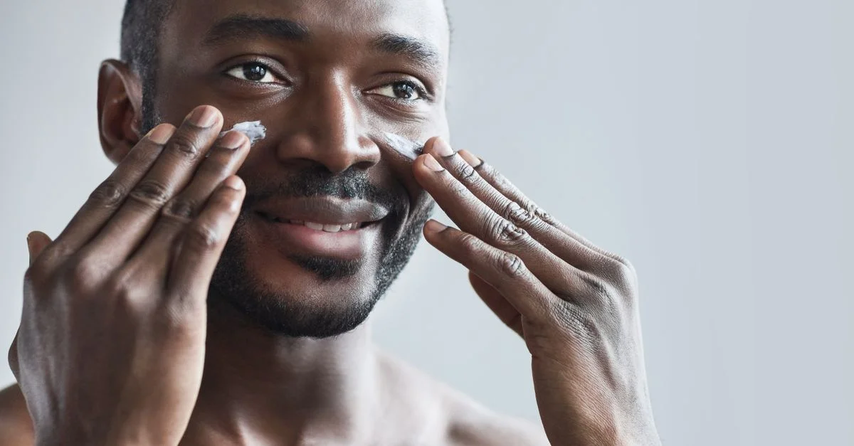 Homme souriant appliquant de la crème pour le visage dans le cadre de sa routine quotidienne de soins de la peau pour une peau saine.