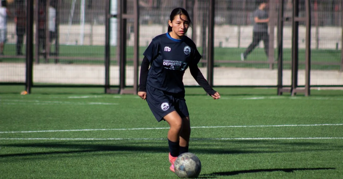 Une jeune athlète joue au football sur un terrain extérieur verdoyant en journée.