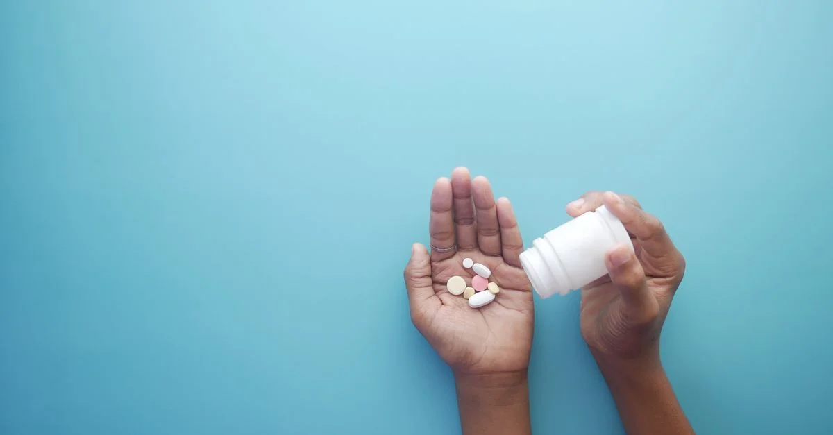 Mains versant des pilules d'une bouteille sur un fond bleu, représentant les soins de santé et les médicaments.