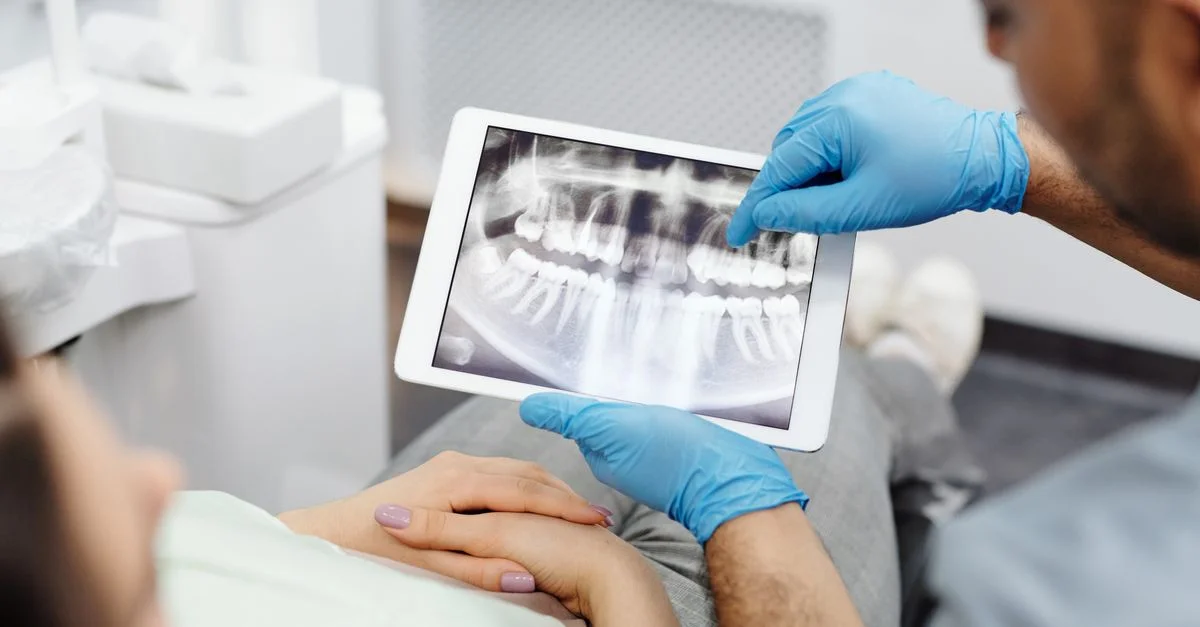 Dentiste examinant une radiographie dentaire avec un patient à l'aide d'une tablette, mettant en avant les soins dentaires modernes.