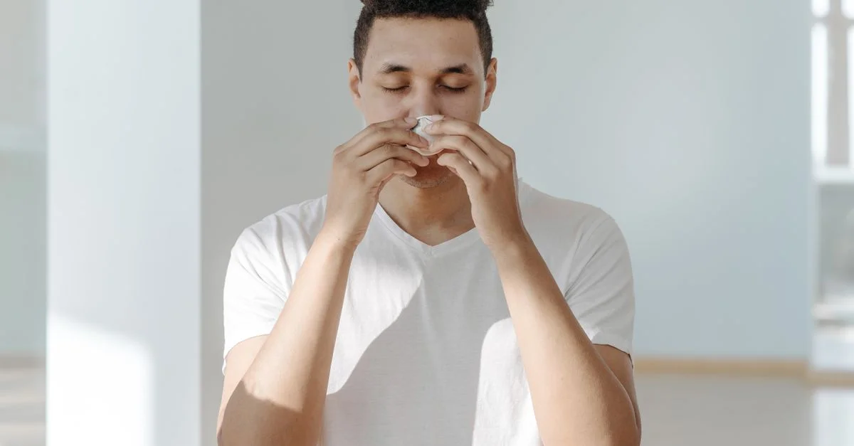 Un homme éternuant dans un mouchoir, illustrant les symptômes de la grippe ou des allergies.