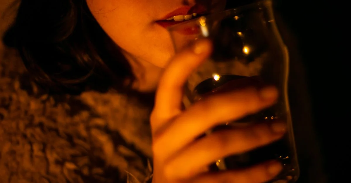 Une femme tenant un verre, éclairée par une lumière chaude et moody, créant une atmosphère intime.