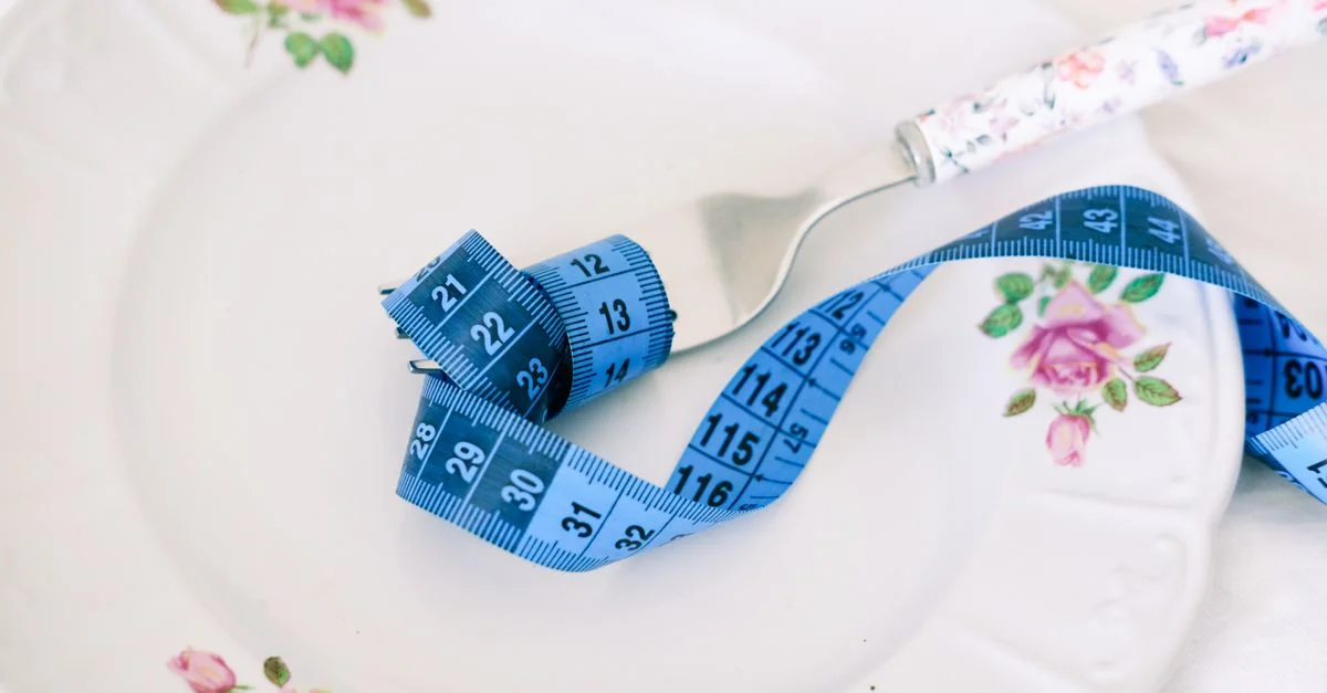 Une assiette florale avec une fourchette et un ruban à mesurer bleu symbolisant un régime ou une alimentation saine.