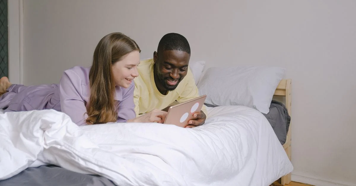 Un couple interracial heureux profitant de moments ensemble à l'intérieur, utilisant une tablette numérique dans leur chambre confortable.