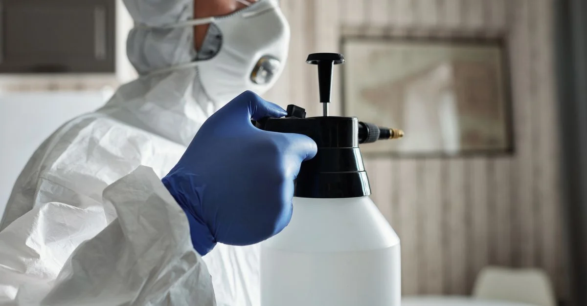 Une personne en équipement de protection avec des gants et un masque facial utilisant un flacon pulvérisateur pour désinfecter à l'intérieur.
