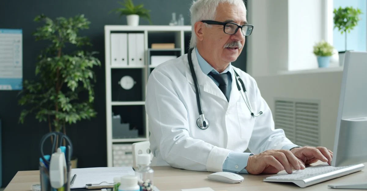 Un médecin âgé tape sur un clavier dans un cabinet médical moderne.