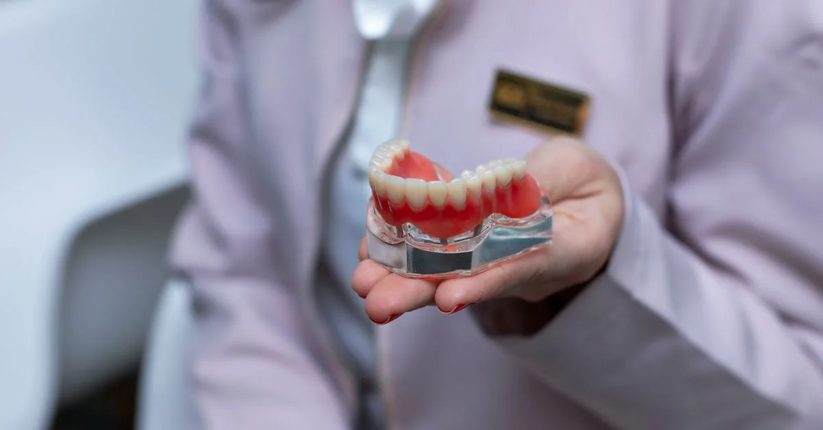 Dentiste en blouse de laboratoire tenant un modèle dentaire à l'intérieur pour l'éducation des patients.