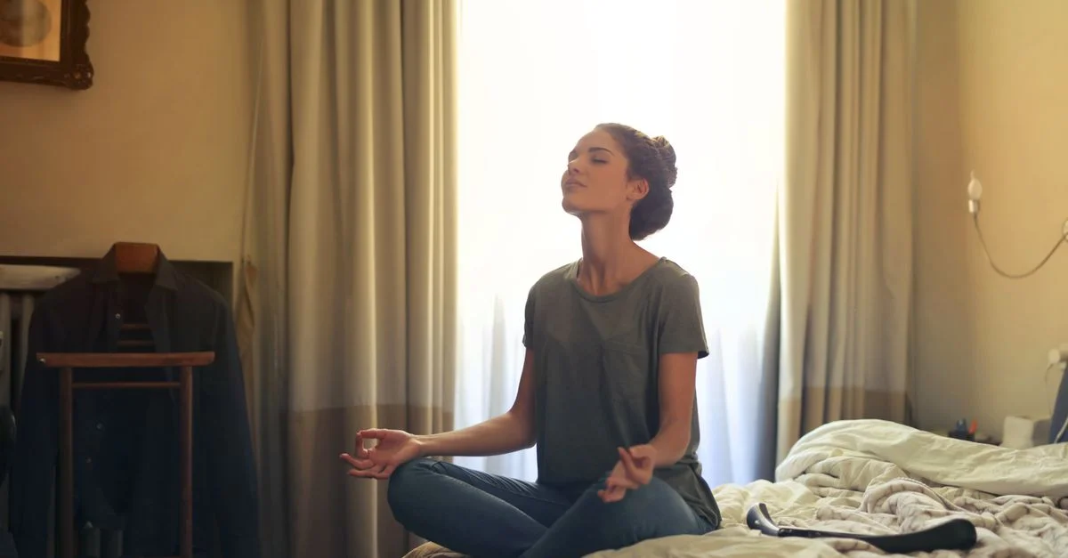Femme adulte pratiquant la méditation sur son lit dans une atmosphère calme.