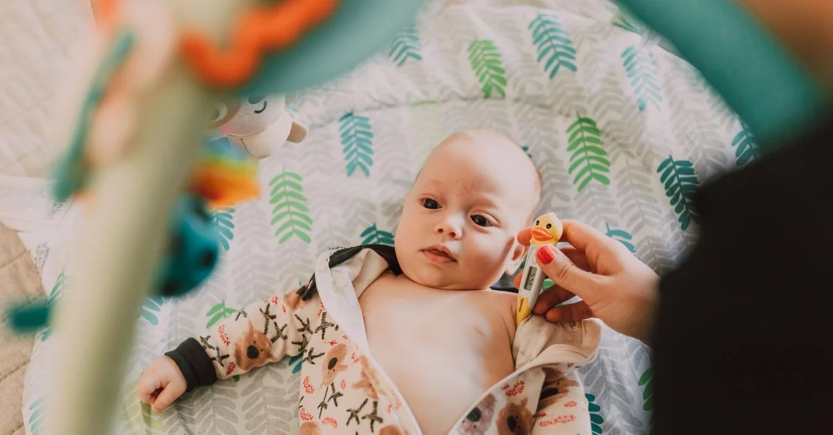 Bébé mignon allongé à l'intérieur avec un thermomètre, portant une grenouillère à motifs.