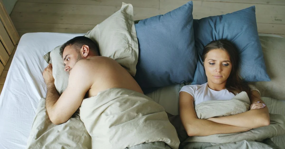 Un couple tendu, allongé séparément dans le lit, reflète les tensions de leur relation.