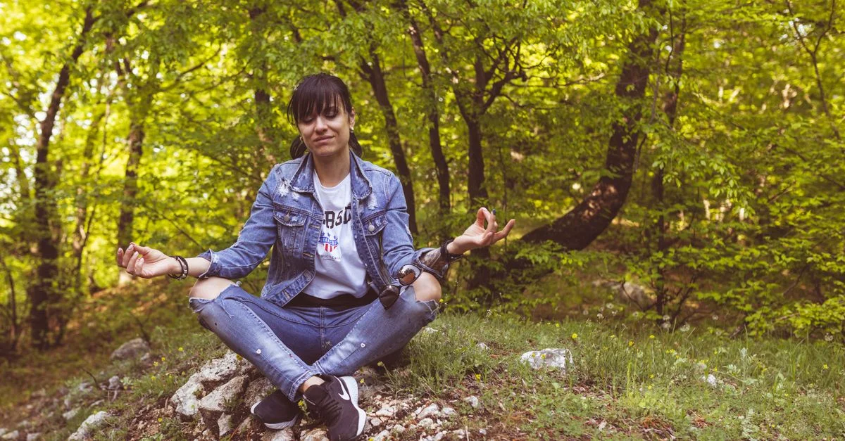 Une femme médite paisiblement dans une forêt verdoyante, dégageant calme et détente.