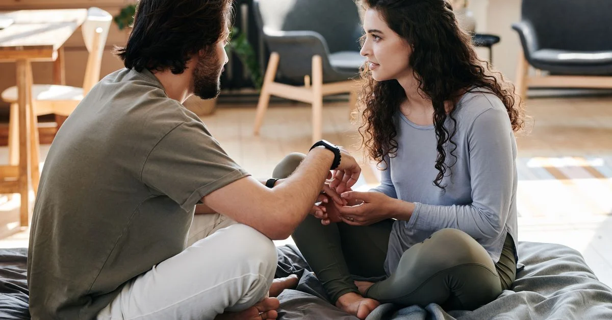 Un couple assis près l'un de l'autre sur un lit, engagé dans une discussion réfléchie dans un cadre domestique chaleureux.