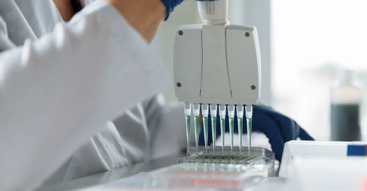 Un scientifique portant une blouse de laboratoire utilise une pipette multicanaux pour la manipulation de liquides dans un environnement de laboratoire.