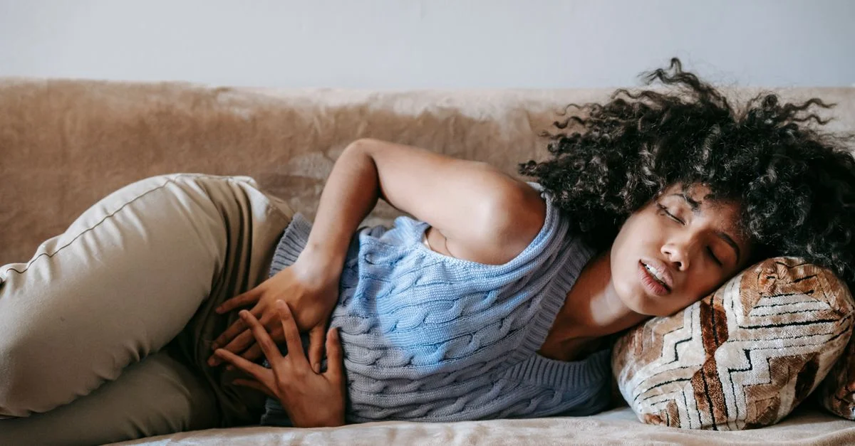 Jeune femme allongée sur le canapé avec des douleurs abdominales, se sentant mal et inconfortable.