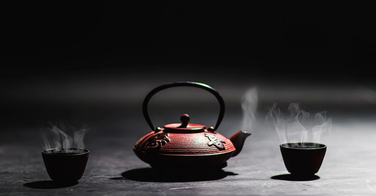 Image minimaliste d'une théière en fonte et de tasses fumantes, parfaite pour des thèmes de culture du thé traditionnelle.