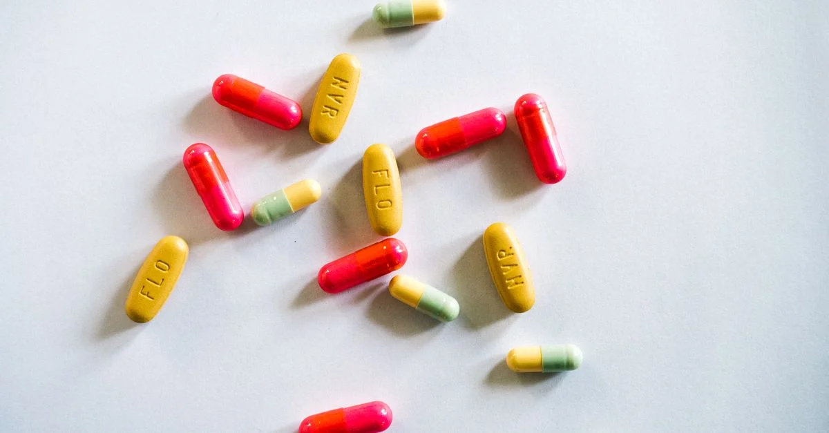 Gélules et comprimés colorés dispersés sur une surface blanche, montrant la variété des médicaments.