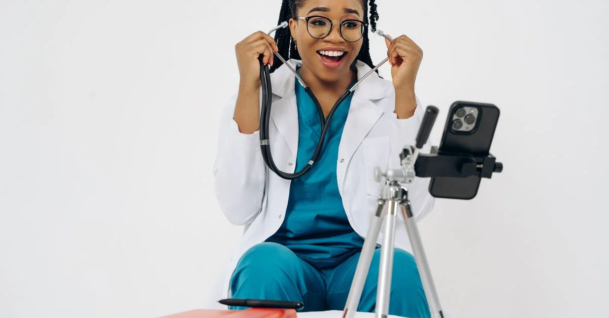 Une médecin joyeuse en blouse et uniforme utilisant un smartphone pour une consultation médicale virtuelle.