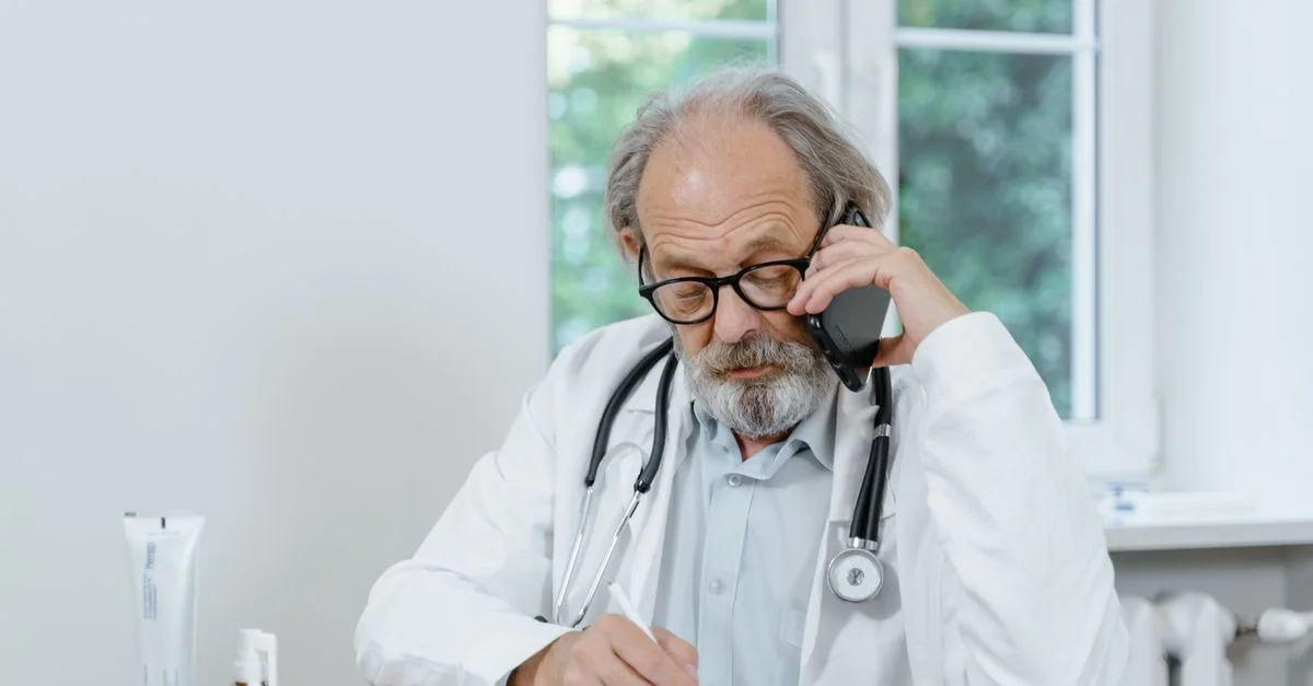 Médecin senior aux cheveux gris prenant des notes lors d'un appel de télémédecine.
