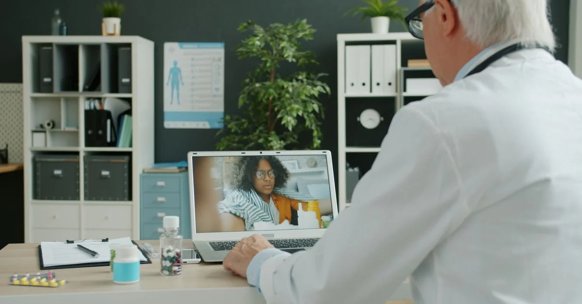 Dans un cabinet moderne, un médecin effectue une consultation virtuelle avec un patient sur un ordinateur portable.