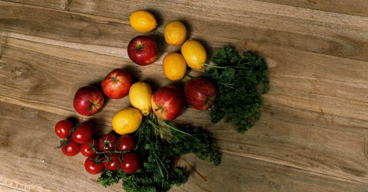 Vue de dessus de pommes, citrons, tomates et persil frais sur une surface en bois.